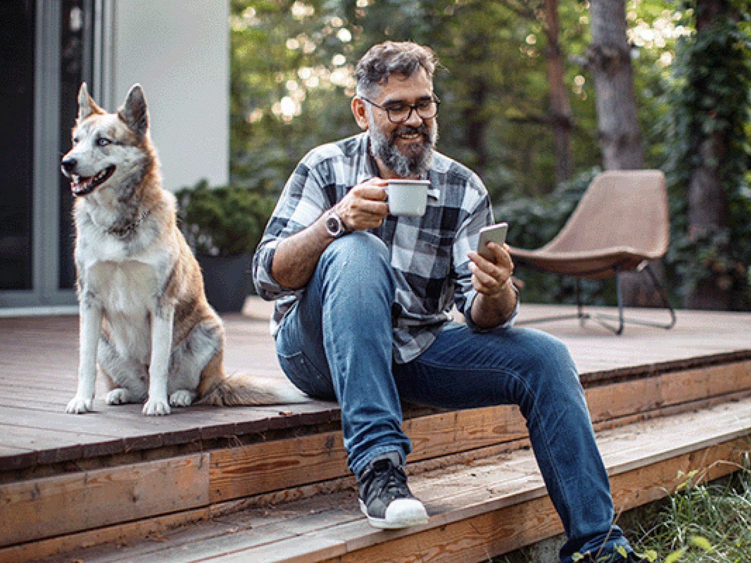 A man sits on a step of a back patio with a large dog next to him.