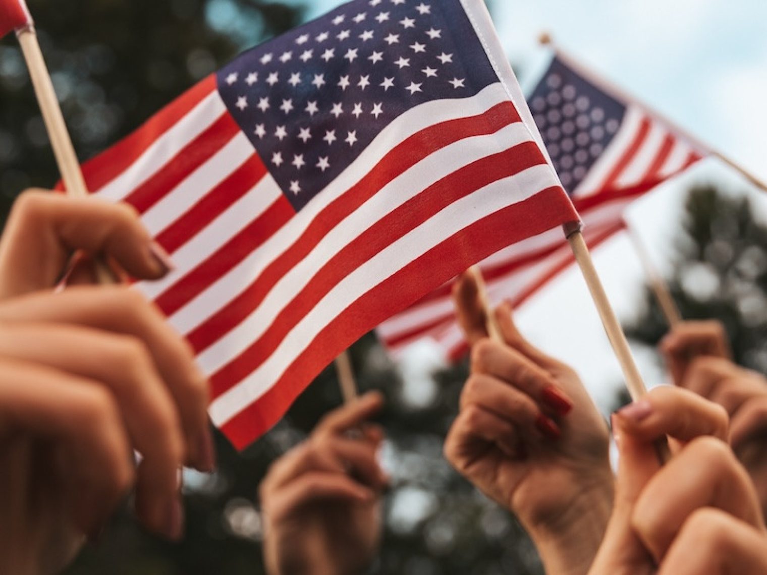 Hands waving small American flags in the air.