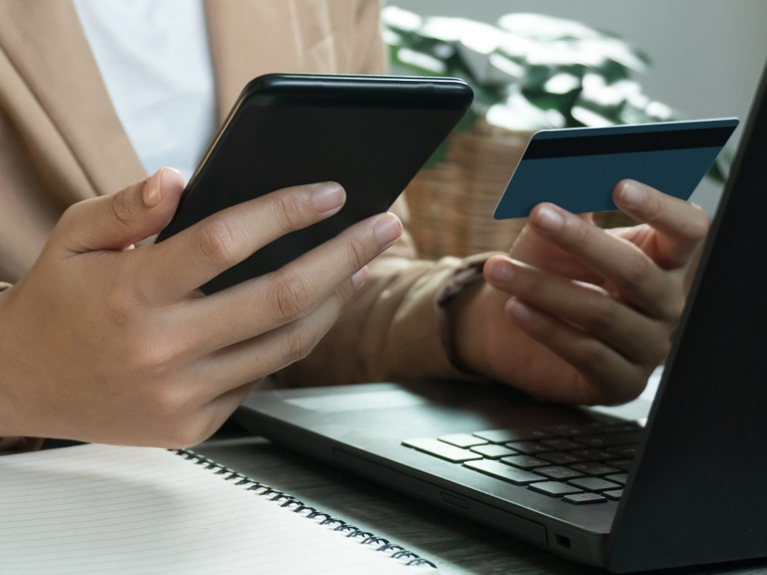 Person sitting in front of laptop holding a phone and credit card.