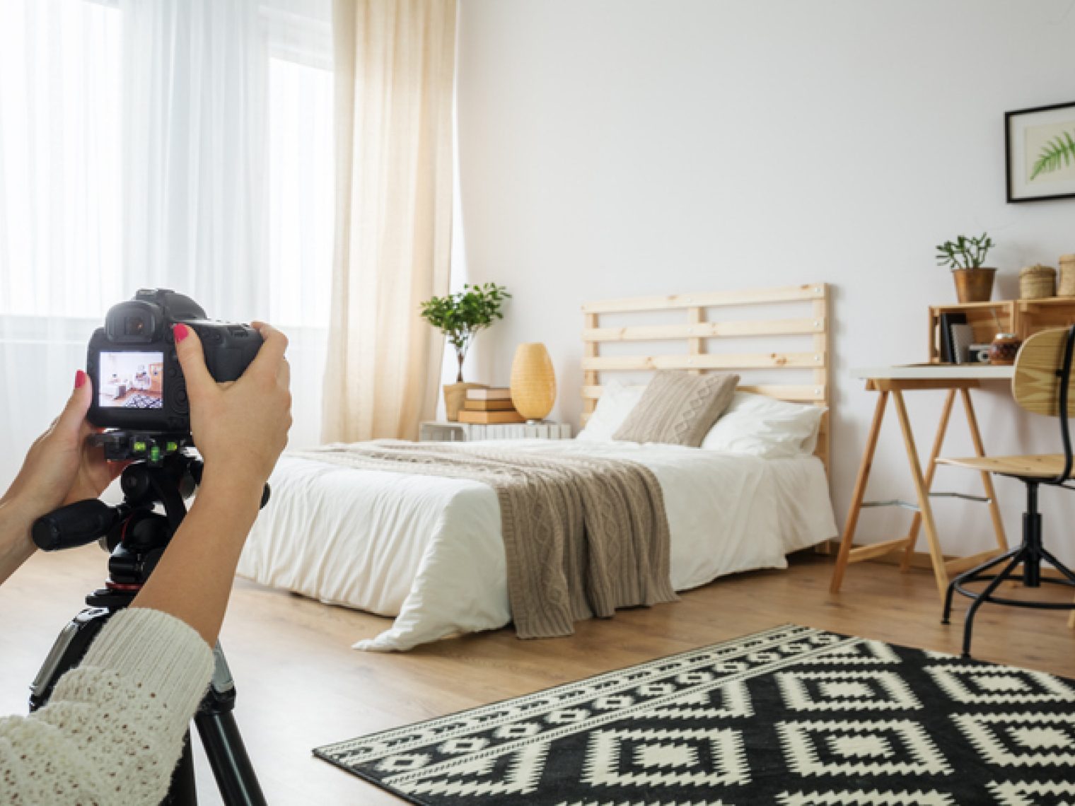 A person is taking a photo with a DSLR camera on a tripod, capturing a well-decorated bedroom with a cozy, modern design, possibly for a real estate listing.