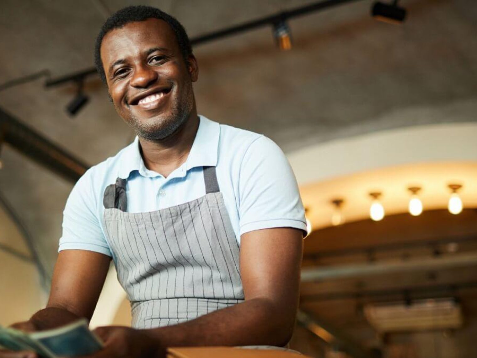 Man wearing an apron smiles at the camera while counting money.