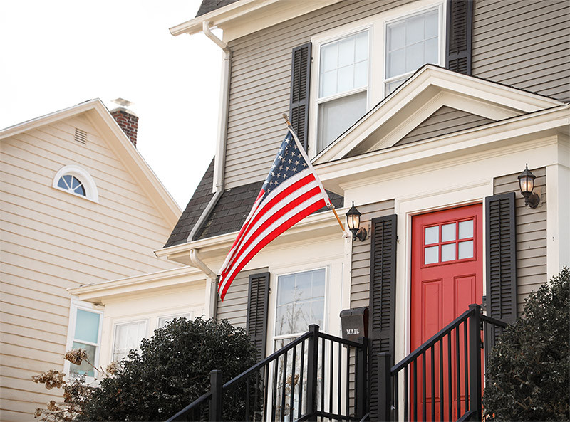 A house with a red door and an American flag displayed on the front porch.