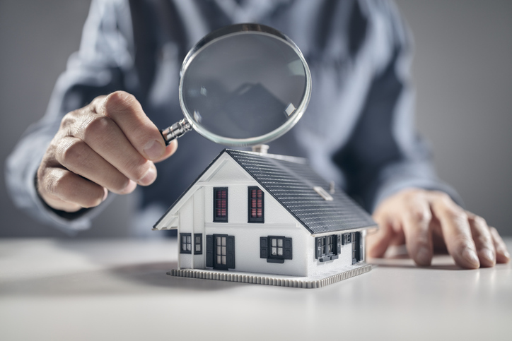 A person examines a model house with a magnifying glass.